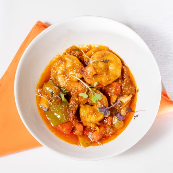 Cross Culture's Indian shrimp curry with bell peppers and microgreens in a white bowl.
