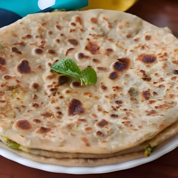 Close-up of a stack of golden-brown Indian parathas, garnished with fresh mint leaves on a white plate.
