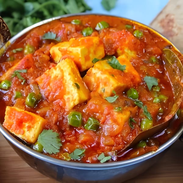 Close-up of a bowl of vibrant Indian matar paneer with green peas and paneer cheese cubes.