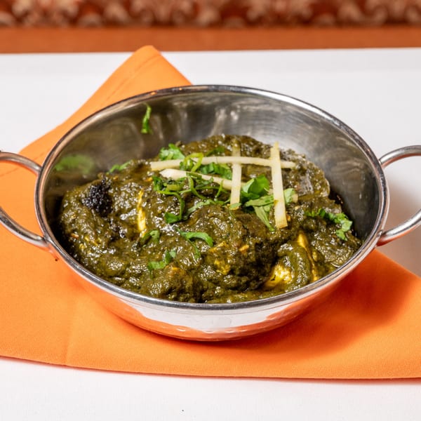 Palak Paneer, a vibrant green Indian spinach and cheese dish, in a metal bowl on an orange napkin.