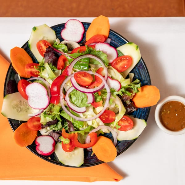 Fresh garden salad with lettuce, tomatoes, cucumbers, radishes, carrots, and red onion, with dressing.
